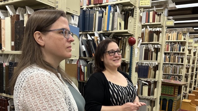 two women standing with shelves of books behind them