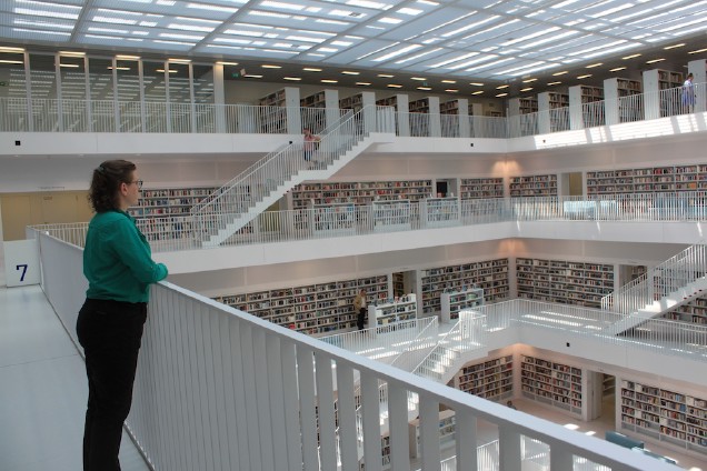 woman standing at a railing looking out over several floors of a modern library with shelves of books